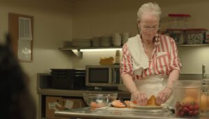 An older woman prepares a dessert in a kitchen.